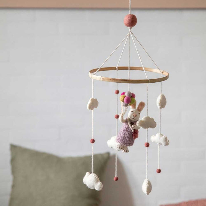 Ein Baby-Mobile „Hase Mädchen mit Luftballons“ von Gry &amp; Sif hängt mit Wolken und kleinen Bällen verziert von der Decke und steht vor einer weißen Backsteinwand.