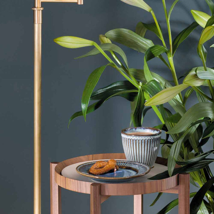 Eine goldene Stehlampe steht neben einem hölzernen Beistelltisch mit einer Pflanze, einer entkernten Keramikschale und einem Teller mit zwei GreenGate - Alice Eierbechern.